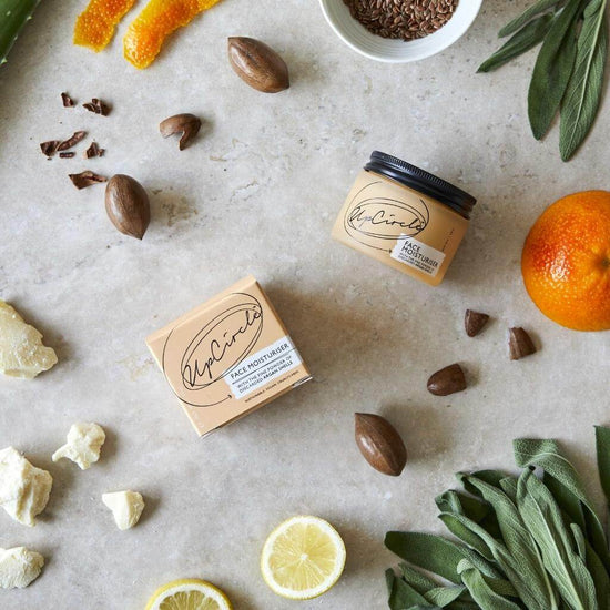 Upcircle Face Moisturiser with jar and box laying on a table and its incorporated raw ingredients on display.