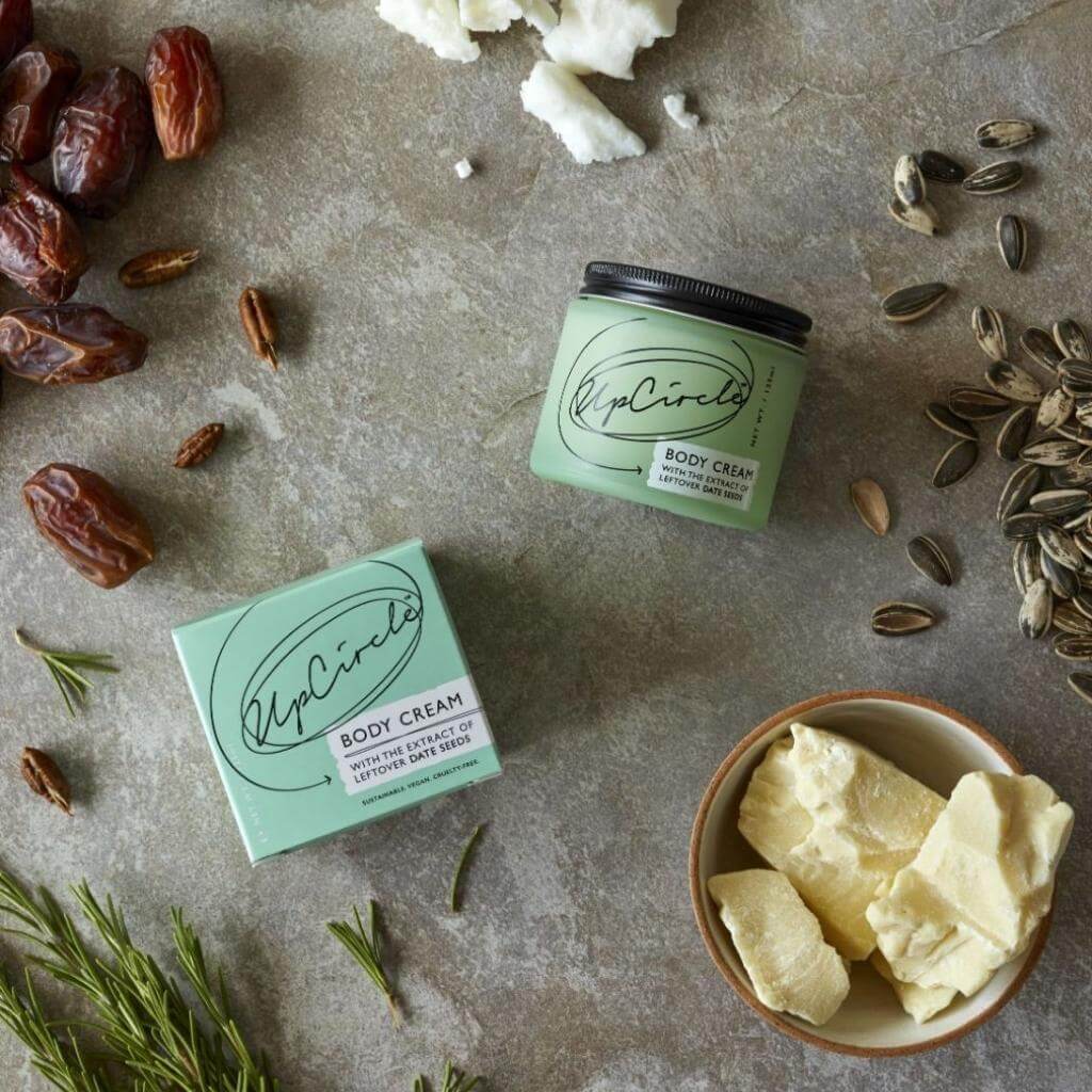 UpCircle - Body Cream on a table with cardboard packaging, and incorporated raw ingredients all displayed.