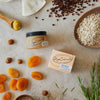 Upcircle Cleansing Face Balm jar and its box on a bench with its incorporating raw ingredients on show.