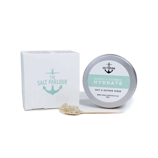 The Salt Parlour Seaweed & Cucumber Scrub HYDRATE salt and sulphur scrub with wooden spoon holding a small amount of salt scrub. The box and tin are upright on a white background