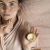 UpCircle - Night Cream jar being held by a model lying on a bed, and applying the cream to her face.
