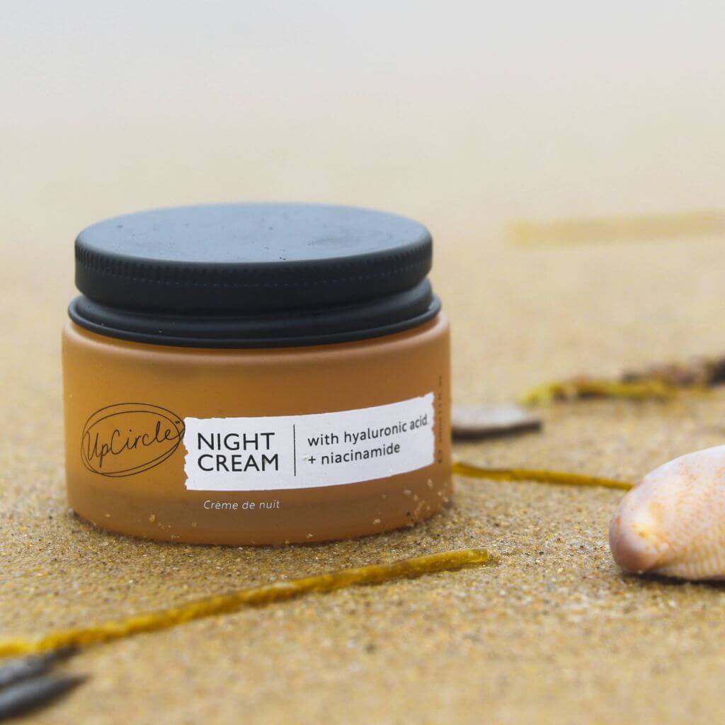 UpCircle - Travel sized Night Cream with repurposed blueberry extract. Lifestyle image from the beach. Sand in the background. Lid on.
