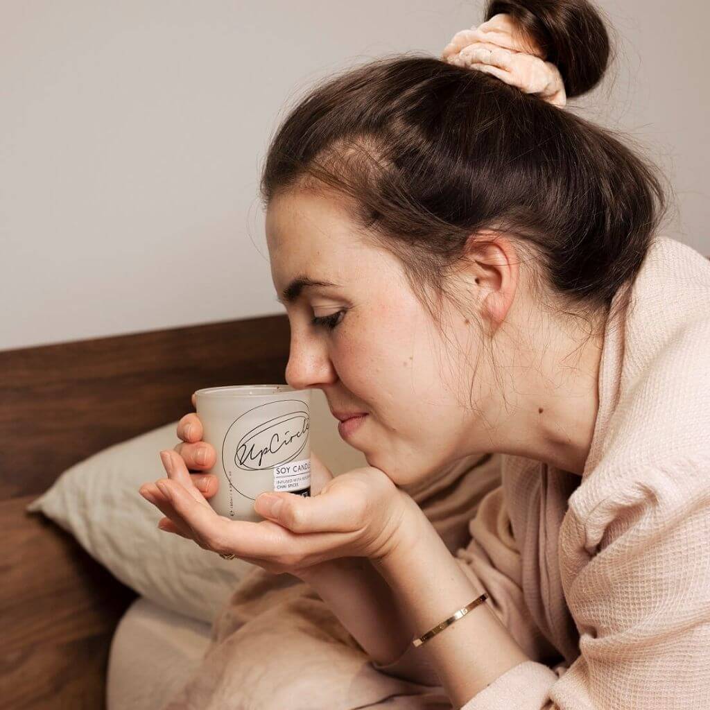 Upcircle Chai Latte Natural Soy Candle Lifestyle image. Model smelling chai candle while holding the candle in her hands.