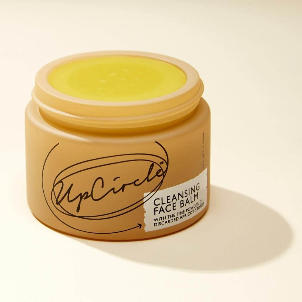 Upcircle Cleansing Face Balm without lid and bright yellow balm is visible. On a cream background with a distinct shadow.