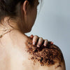 Upcircle Body Scrub with Lemongrass being applied to the shoulder of the model. The coffee grounds colour is dark brown.