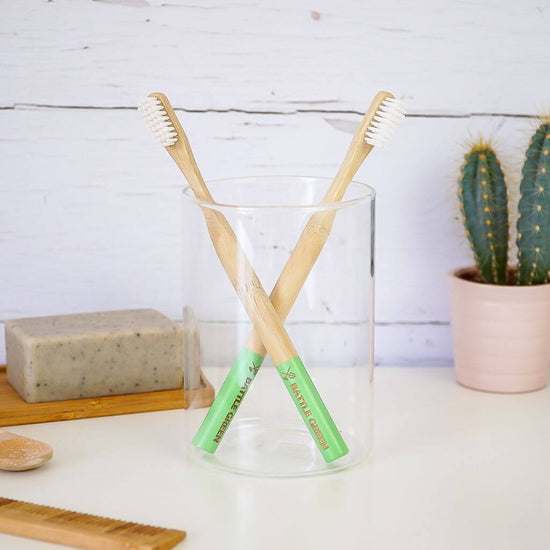 Battle Green Bamboo Toothbrush with Castor Oil Bio Bristles. on display with 2 toothbrushes crossed in glass. on basin.