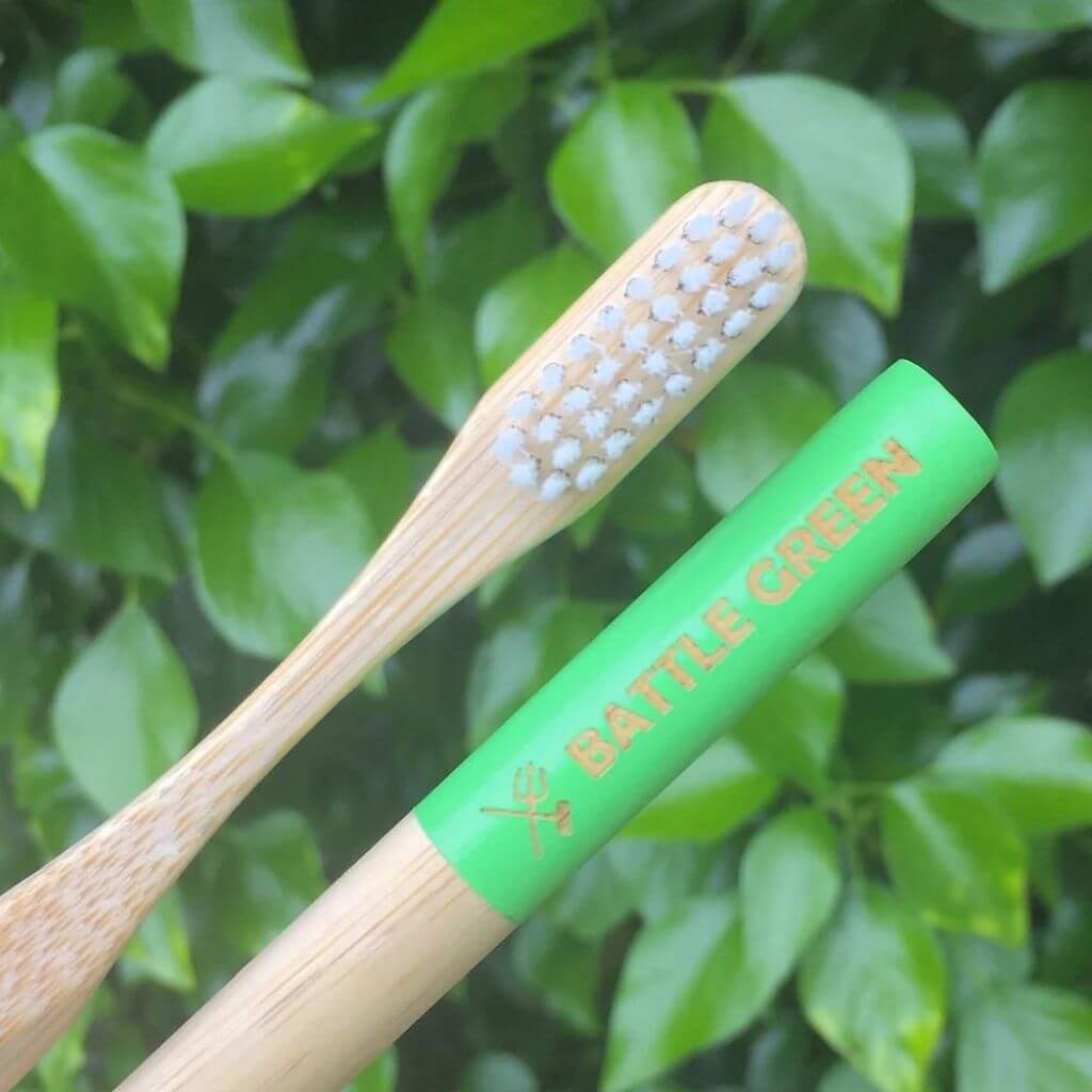 Battle Green Bamboo Toothbrush with Castor Oil Bio Bristles. Lifestyle image with green bamboo in the background.