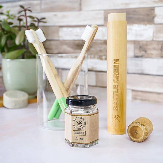 Battle Green Bamboo Toothbrush with Castor Oil Bio Bristles. on basin with toothbrush holder and other products. lid off.
