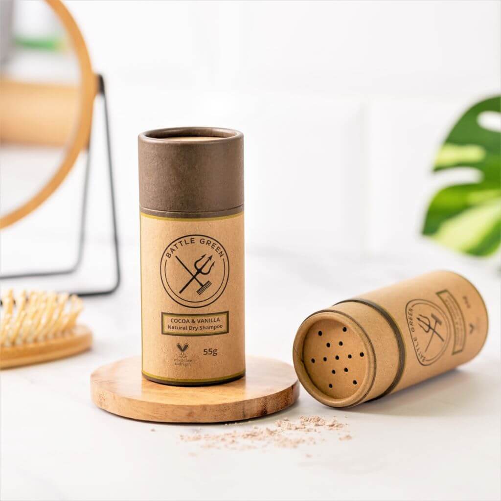 Battle Green Cocoa & Vanilla Dry Shampoo Shaker Pot. Display with 2 pots. one with lid off showing the top of the cardboard tube, and one with lid on. Great for traveling and to boost volume in your hair. Dark hair.