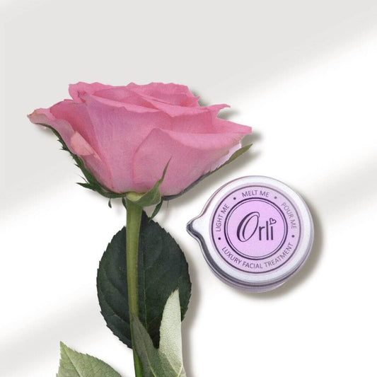 Orli Rose & Neroli Facial Treatment Candle with aluminium tin. on display with a rose geranium. Ultimate face care treatment at home.