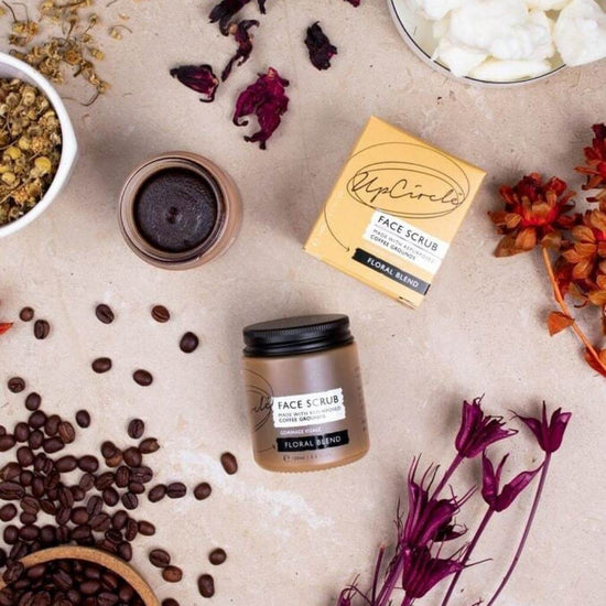 Upcircle Face Scrub Floral Blend laid on a table with its incorporating raw ingredients on show around the jar, box and another jar with the product visible.