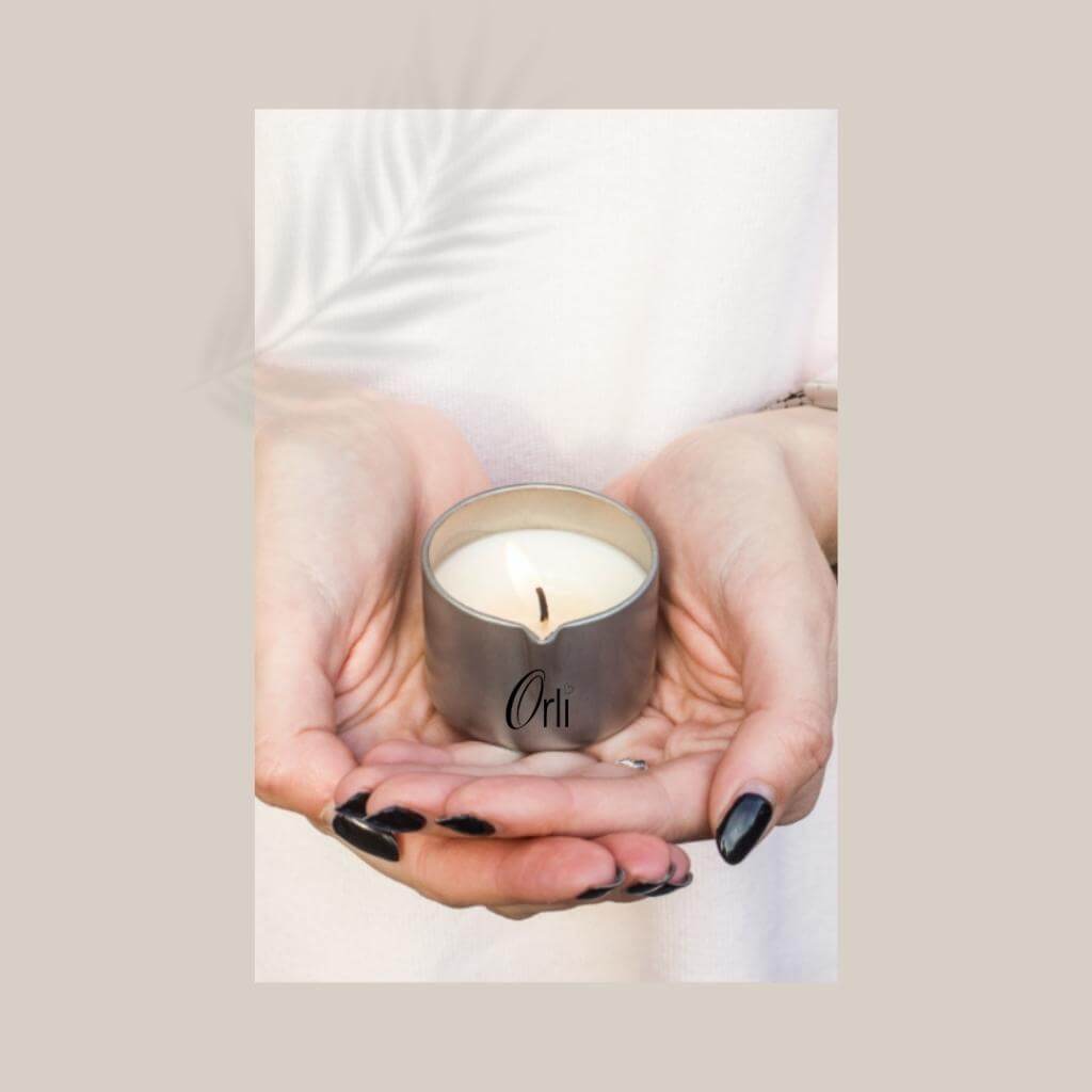 Orli Massage Candle in Aluminium tin being held in the hands. Lid Off.