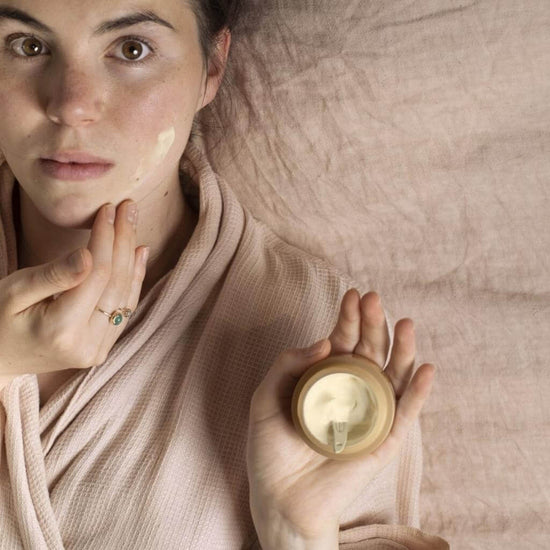 UpCircle - Night Cream jar being held by a model lying on a bed, and applying the cream to her face.