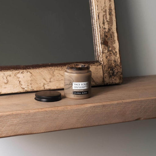 Upcircle Face Scrub Floral Blend on a wooden shelf with its lid off and a mirror behind.
