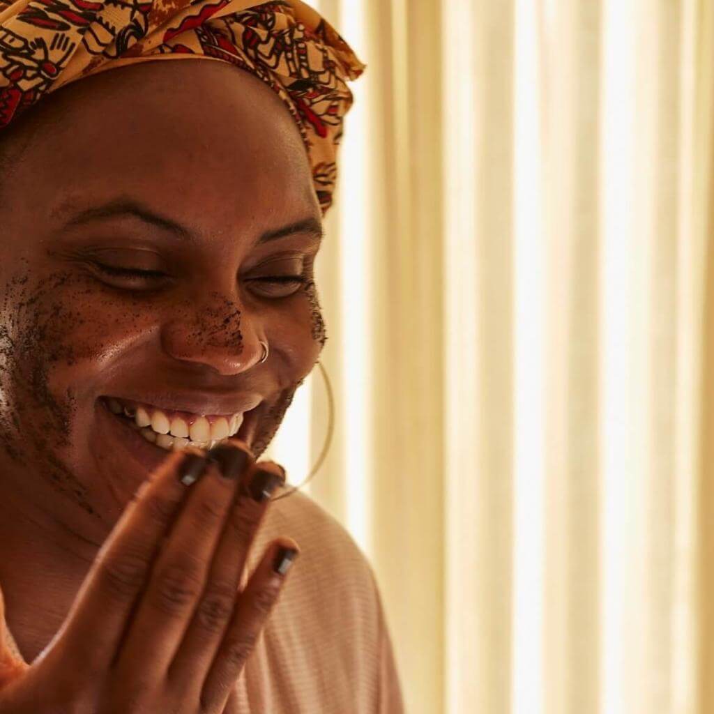 Upcircle Face Scrub Floral Blend being applied by a model on her smiling face. The coffee grounds are visible in the scrub.