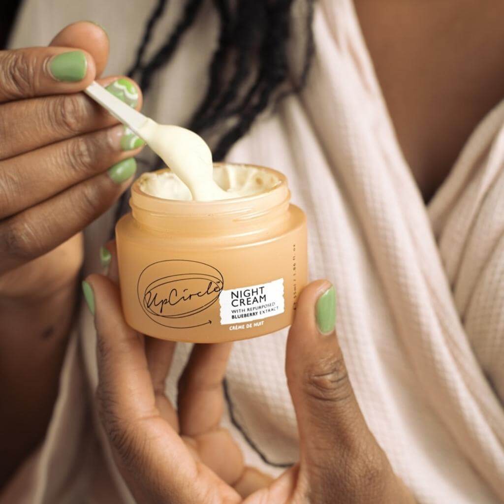 UpCircle - Night Cream jar without lid being held by a model using a scoop to extract the cream.