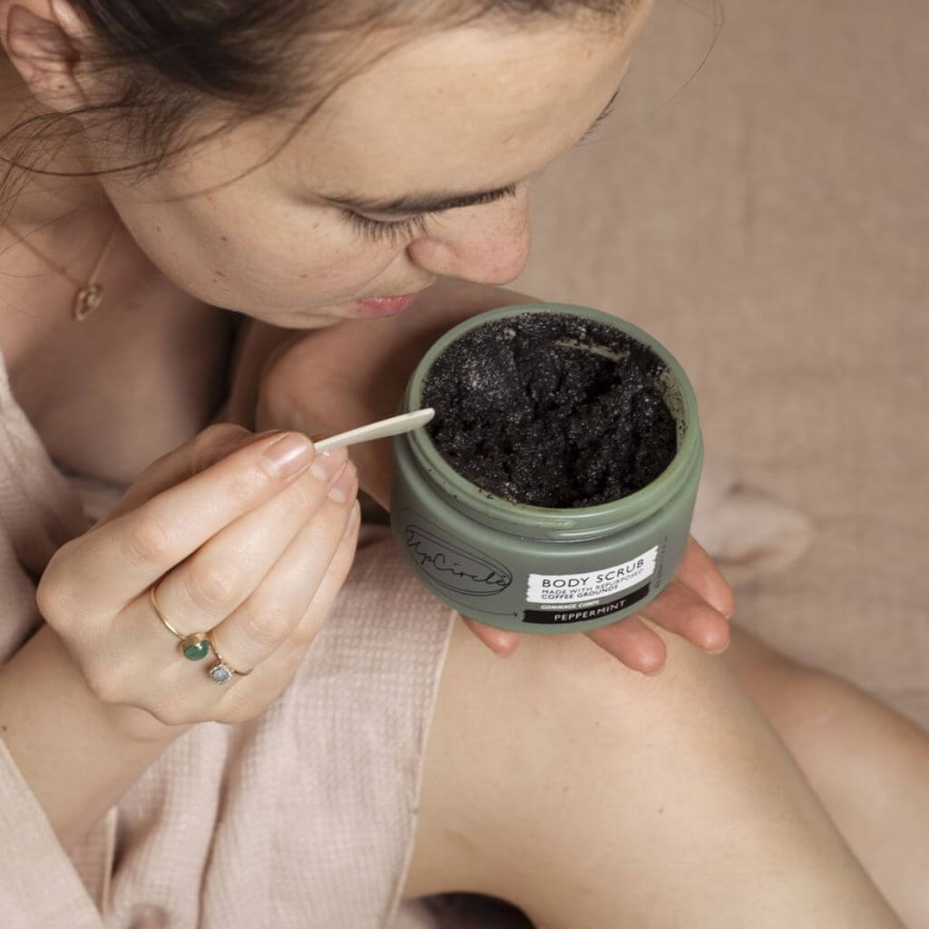 Upcircle Body Scrub with Peppermint jar with lid off, with a model looking in the product after stirring.