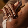Upcircle Body Scrub with Peppermint being applied to the shoulder of the model. The coffee grounds colour is dark brown.
