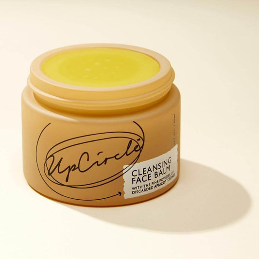 Upcircle Cleansing Face Balm without lid and bright yellow balm is visible. On a cream background with a distinct shadow.