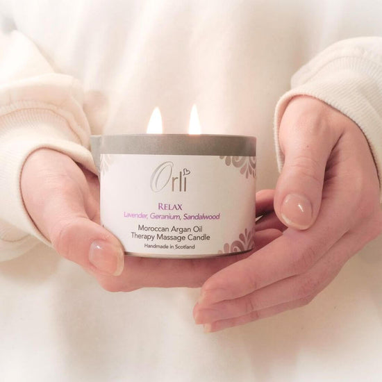 Orli Relax Therapy Massage Candle with aluminium tin. being held in the hands. 160ml tin on show with twin candle flames. Elegant oil to massage the body, mind and soul.