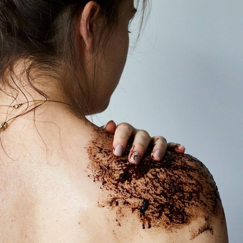 Upcircle Body Scrub with Lemongrass being applied to the shoulder of the model. The coffee grounds colour is dark brown.