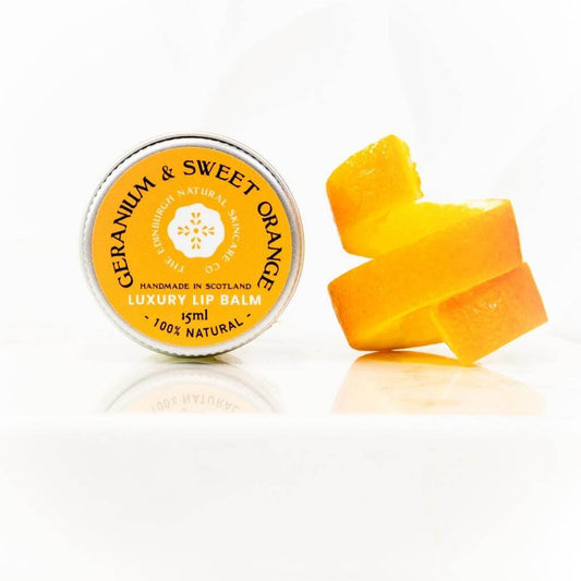 The Edinburgh Natural Skincare Co. Geranium and Sweet Orange Luxury Lip Balm. A jar on its side with an slither of orange peel beside it.
